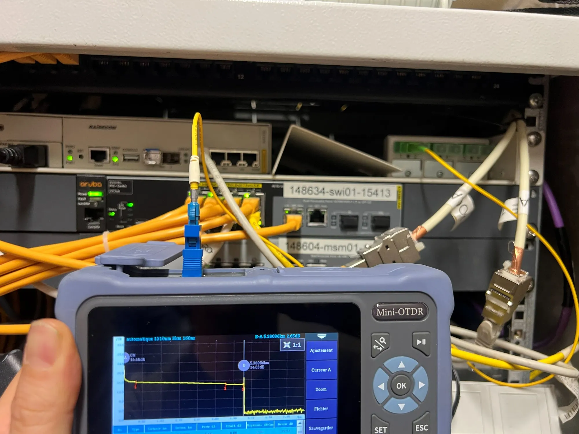 Réflectomètre optique en cours de mesure devant une baie de brassage